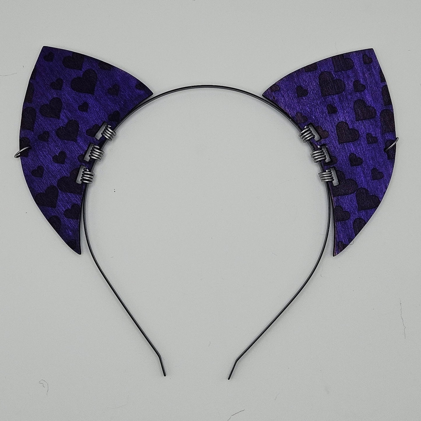 Black headband with purple cat ears featuring black heart patterns on a light gray background